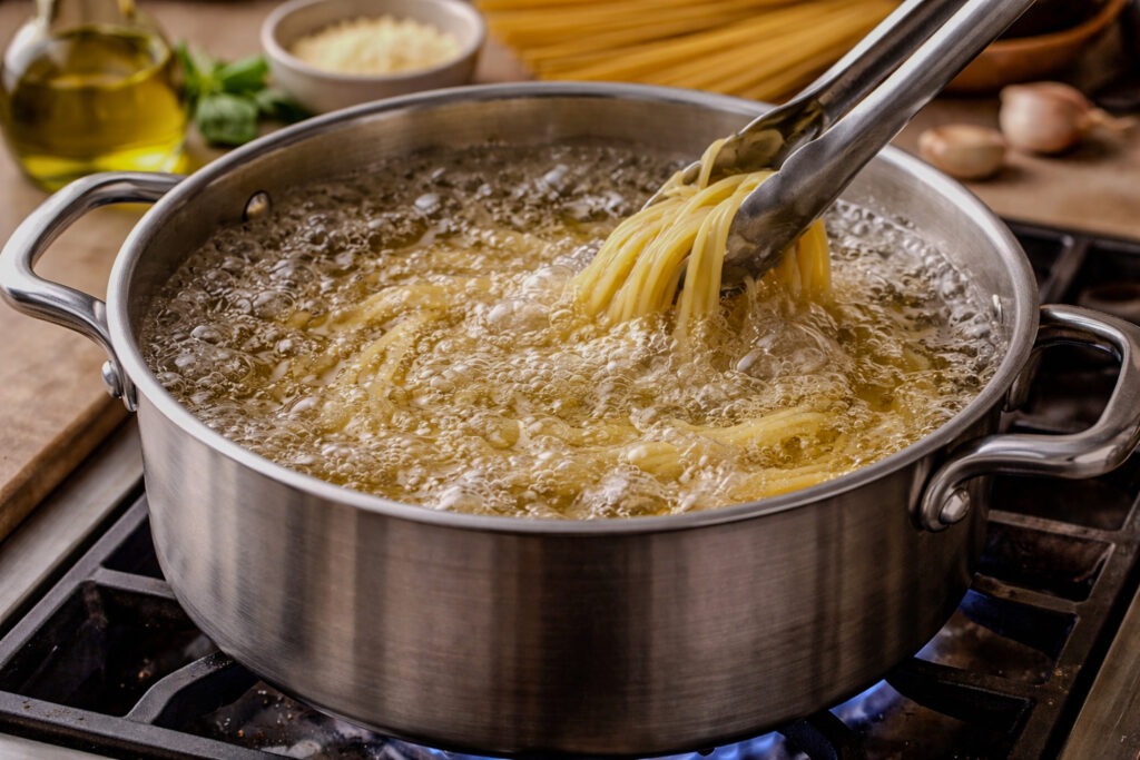 Pot of water at a rolling boil on a stovetop with pasta cooking, demonstrating the boiling cooking technique.