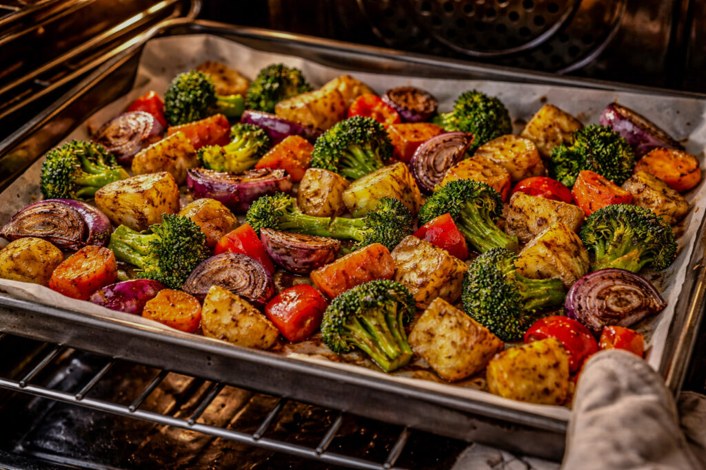 Roasting mixed vegetables on a sheet pan in the oven, showing caramelized broccoli, potatoes, carrots, and red onions.