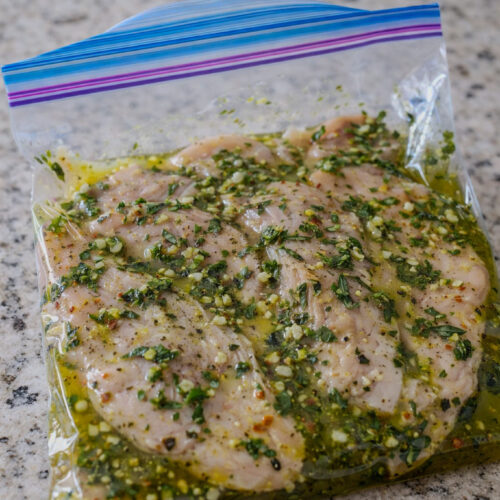 Grilled chicken breasts topped with fresh basil dressing on a serving plate