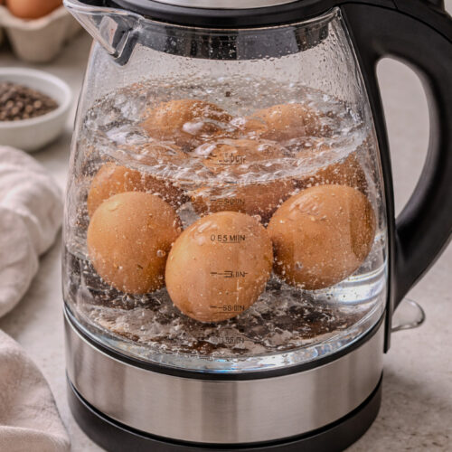 Eggs submerged in water inside a glass electric kettle before boiling.
