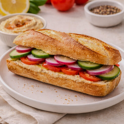 Hummus vegetable sandwich with cucumber, radish, tomato, and red onion on toasted bread.