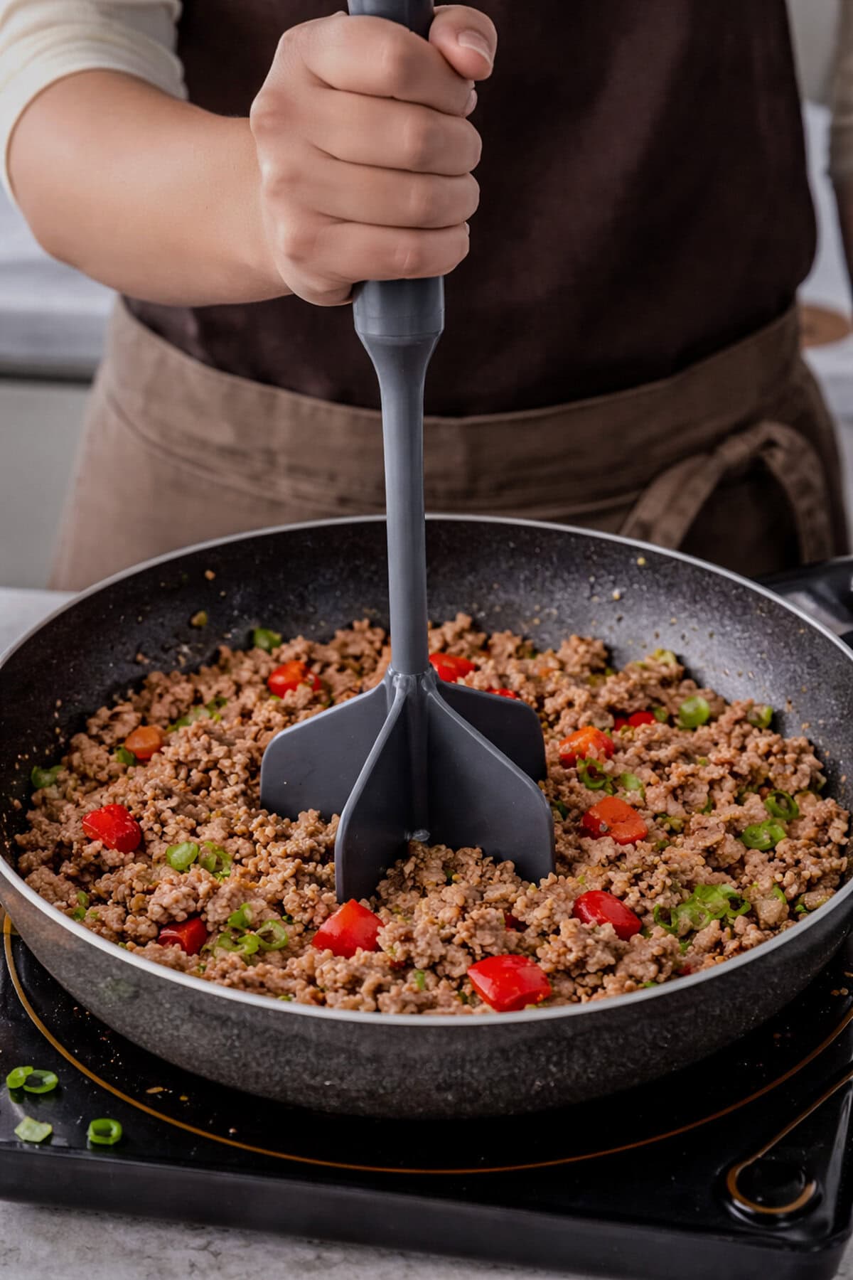 Meat chopper breaking up ground beef in a skillet on the stovetop