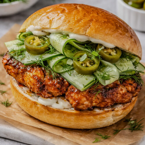 Crispy peri peri chicken sandwich topped with cucumber ribbons, fresh dill, and jalapeños on a toasted bun