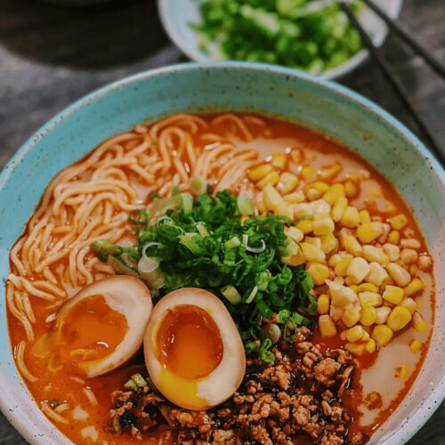 Spicy miso ramen with soft-boiled egg, ground pork, corn, green onions, and noodles in a rich red broth.
