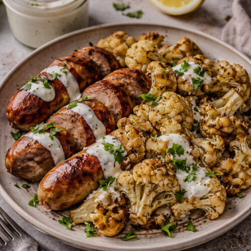 Sheet pan sausage and cauliflower served with lemon garlic yogurt sauce on a plate with sauce jar