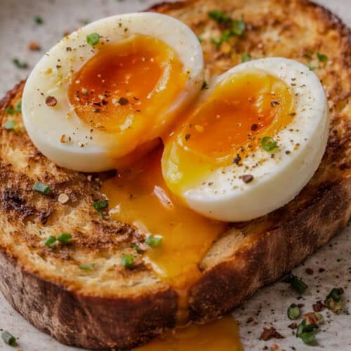 Soft-boiled egg cut in half over toast with runny yolk flowing onto the bread.