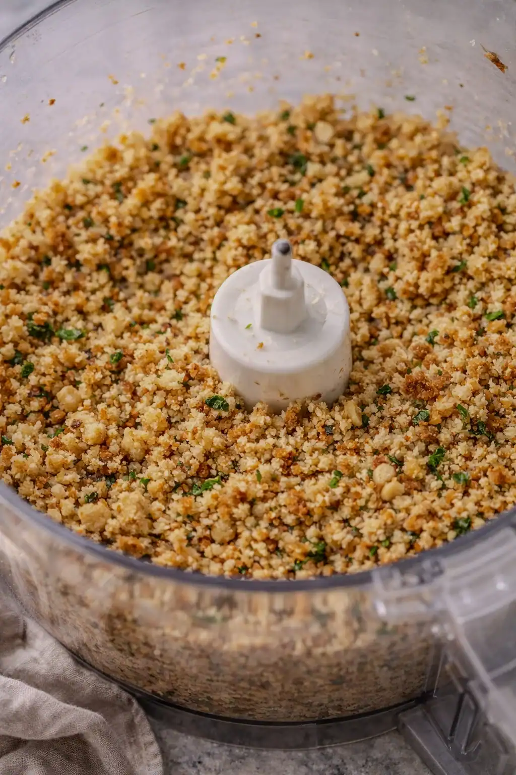 Walnut breadcrumb mixture blended in a food processor, showing a coarse, crumbly texture with herbs mixed throughout.