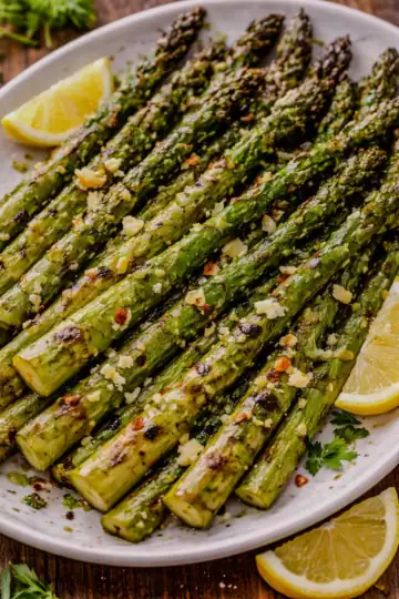 Grilled asparagus with olive oil, garlic, and lemon on a white plate with light char