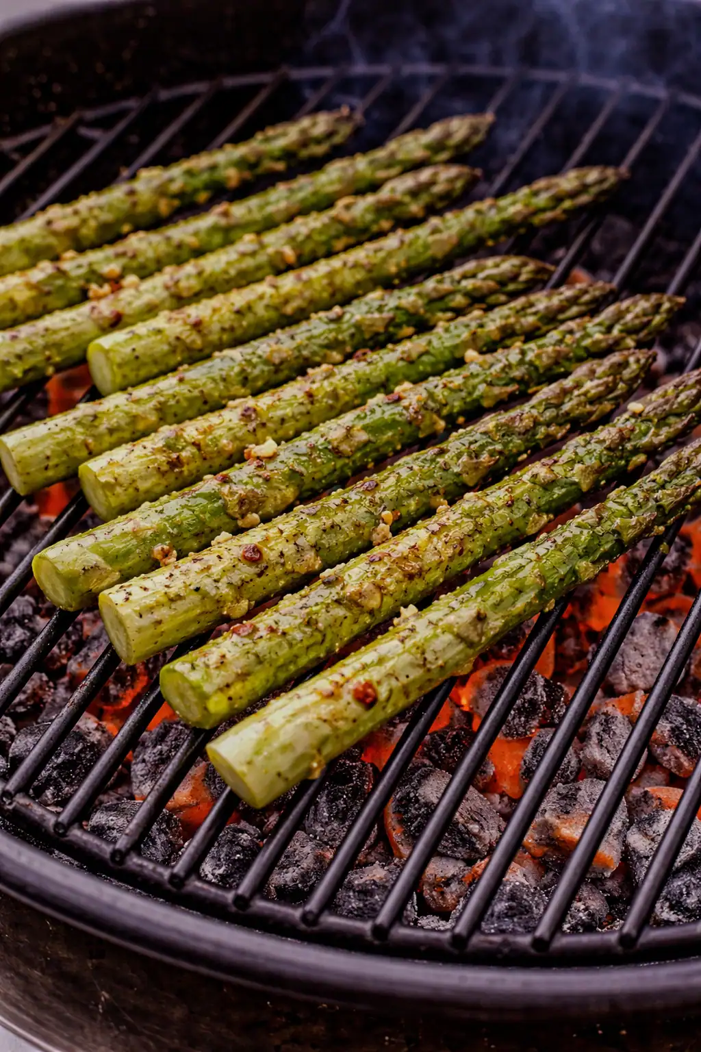 Asparagus spears grilling over hot coals on a barbecue, lightly charred and coated with garlic and olive oil