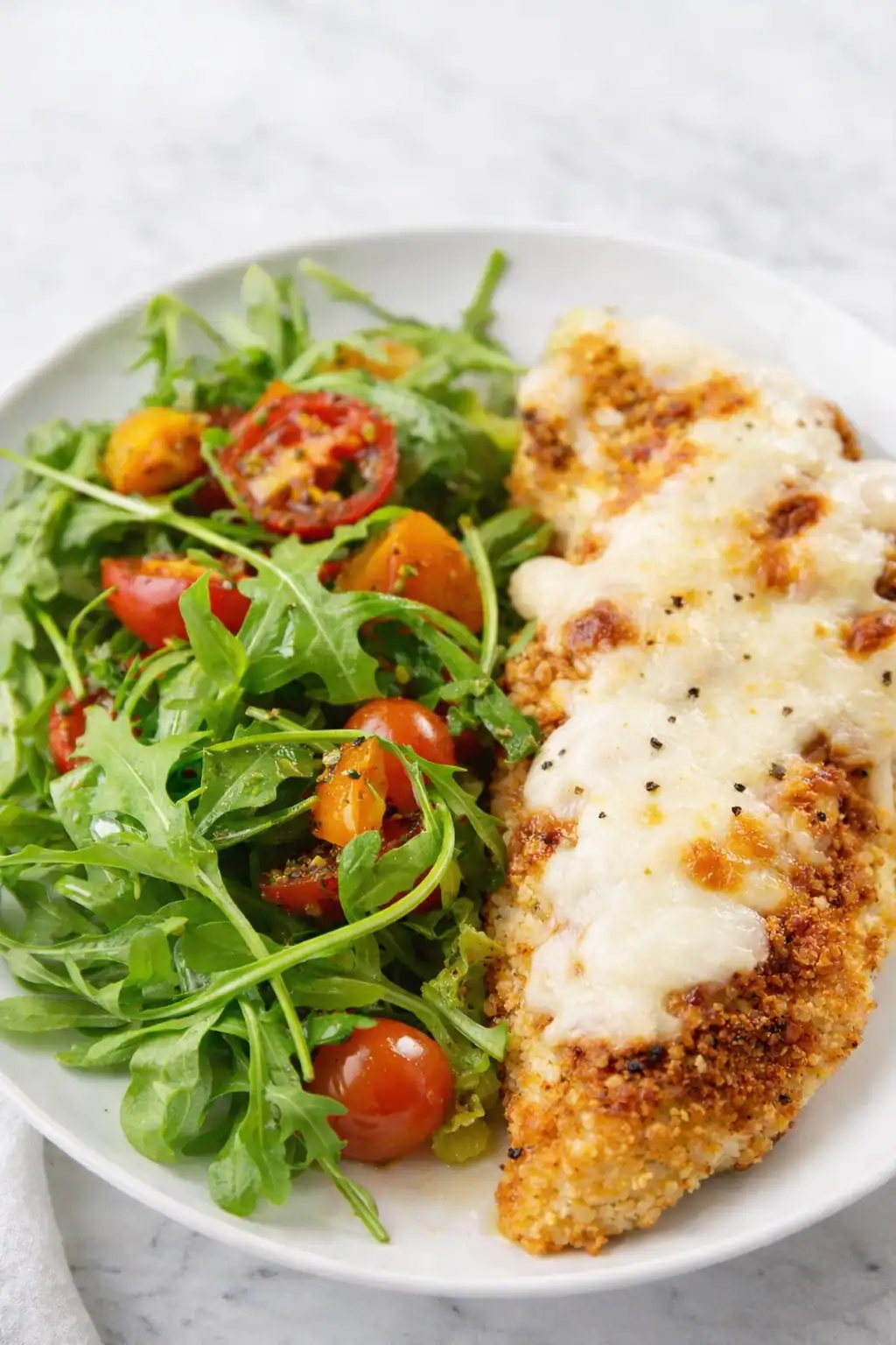 Light baked chicken parmesan with crispy coating, melted mozzarella, and fresh arugula salad with cherry tomatoes