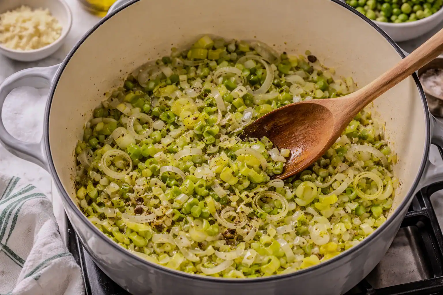 Chopped leeks sautéing in olive oil in a Dutch oven, softened and lightly golden, being stirred with a wooden spoon