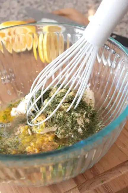 Mixing Mediterranean yogurt marinade with herbs and lemon in a glass bowl.