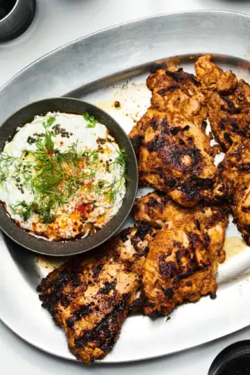 A plate of perfectly grilled chicken pieces accompanied by a creamy herb yogurt sauce, ideal for healthy eating and flavorful dining.
