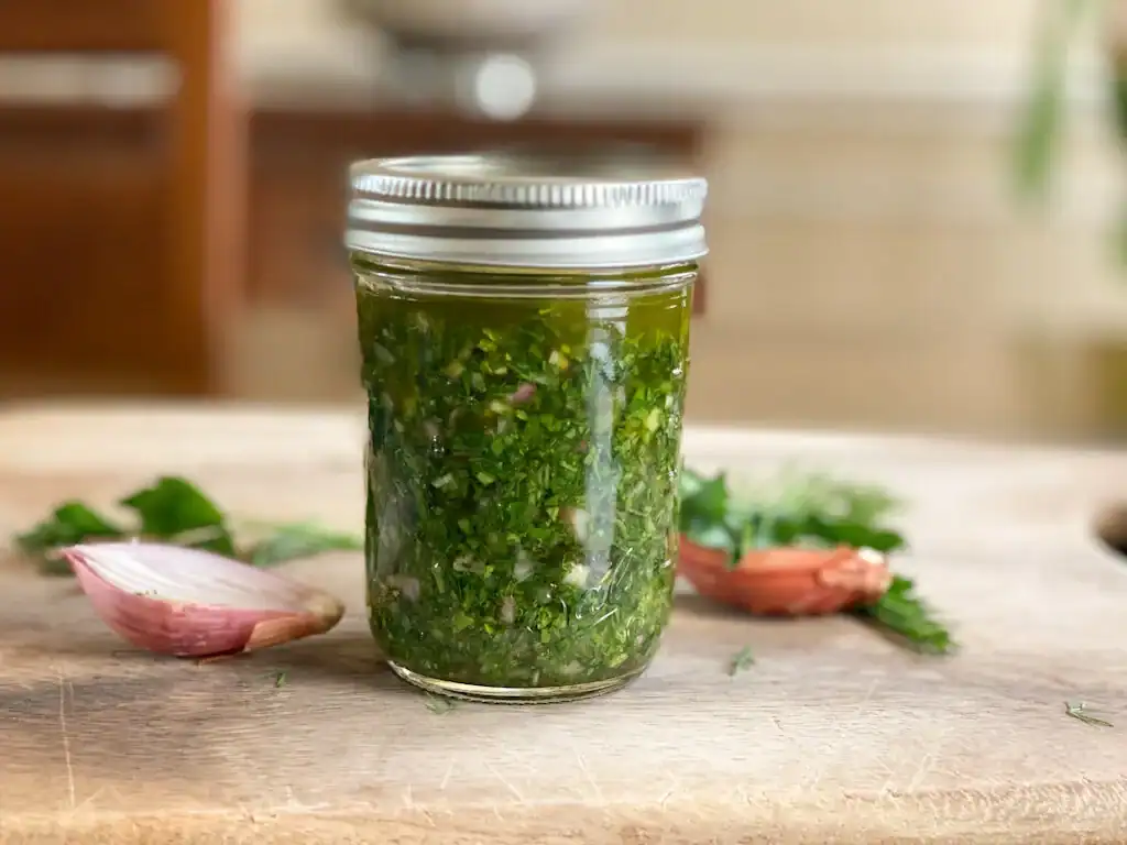 Zhoug sauce in a plain glass jar with a lid, set on a clean surface with no labels or text, ready for refrigeration.